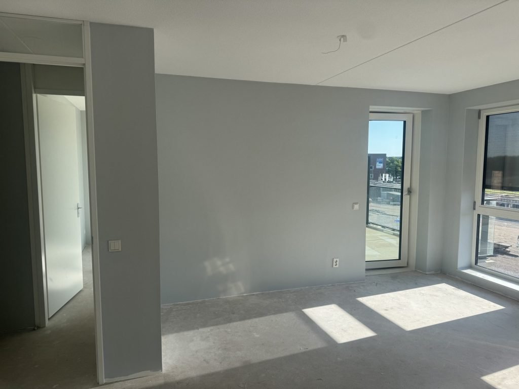 Nieuw appartement met een balkondeur, lichtblauw geverfde wanden en zon op de betonvloer